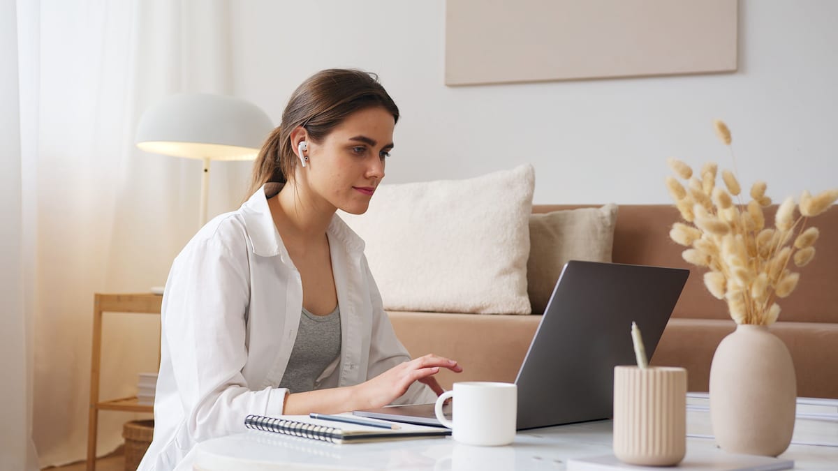 Homeowner at a laptop with a notepad and coffee, reviewing contractor quotes at her living room table
