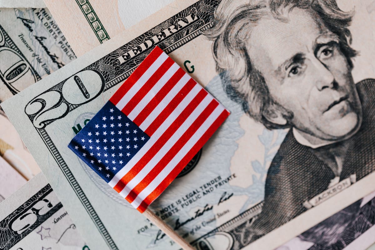 A small American flag on a toothpick laid across a US twenty dollar bill, on a spread of other US currency