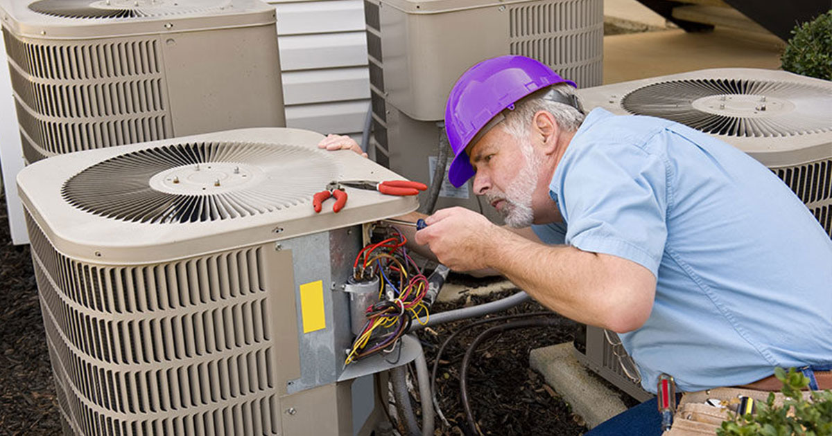 HVAC technician in a hard hat servicing outdoor central air conditioning units