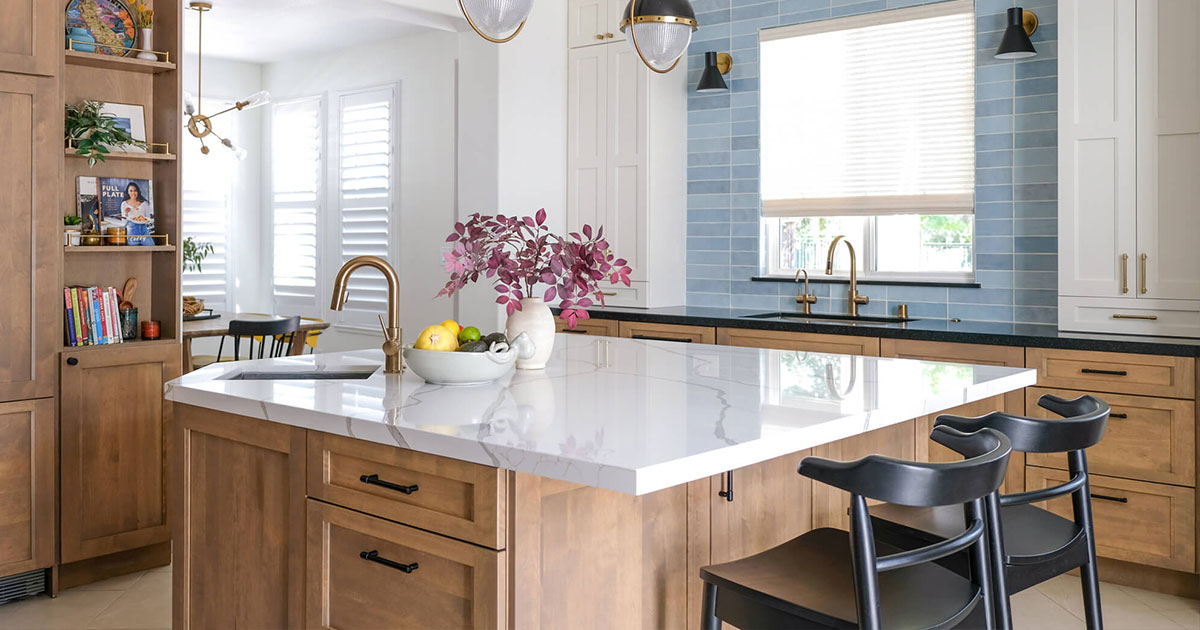 Renovated kitchen with large island, white quartz countertop, natural wood cabinets, and blue subway tile backsplash